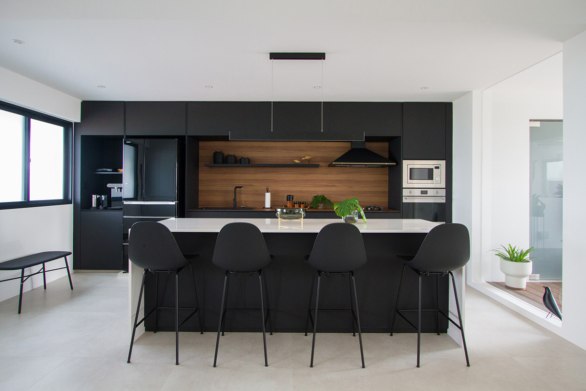 Against the light and airy backdrop of pristine whitewashed walls, the kitchen serves as a anchor point within the communal areas with its striking black aesthetic.