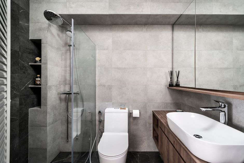 MASTER BATHROOM: Clad in stone-effect homogeneous wall and floor tiles, the bath suite hosts a matching vanity and mirror ledge set of dark wood finishes and thoughtful storage nooks at the shower stall. 