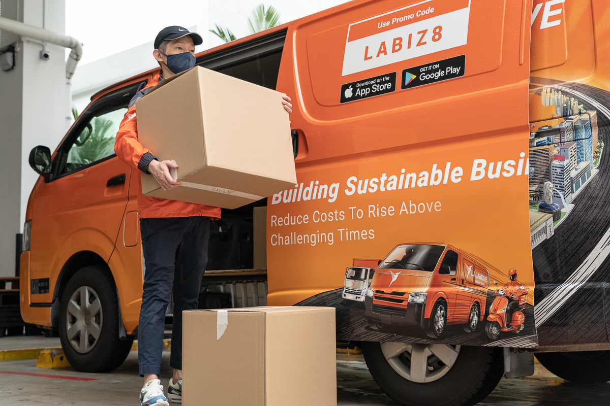 squarerooms lalamove moving service furniture belongings delivery boxes new home transport singapore bernard lim model man in orange uniform standing outside orange van carrying a box with another box on the floor